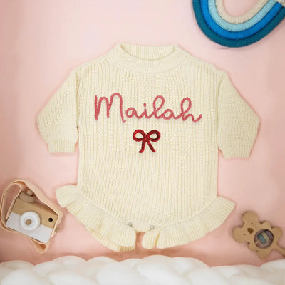 Cream baby romper with 'Mailah' embroidered on a pink background
