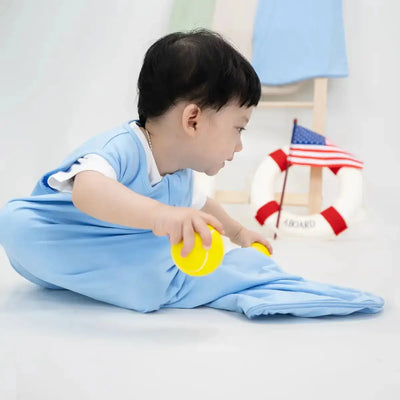 Child in a blue outfit playing with a yellow toy on a light gray surface.