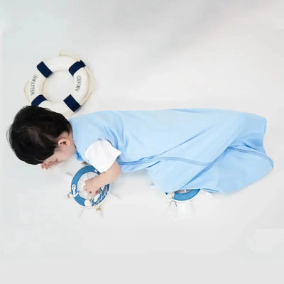 Baby wrapped in a blue blanket playing with a life buoy toy on a white background