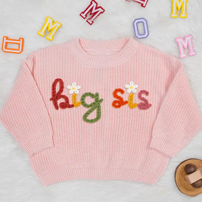 Pink sweater with 'bigsis' text on a light gray background with colorful letters.