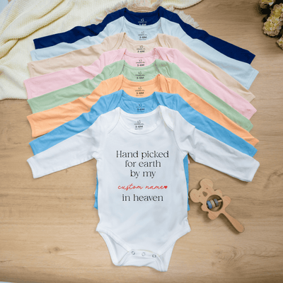 Stack of colorful baby onesies with a white one displaying text on a wooden surface.