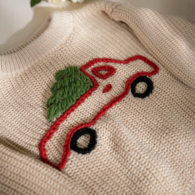 Beige sweater with embroidered red car and green leaf design.