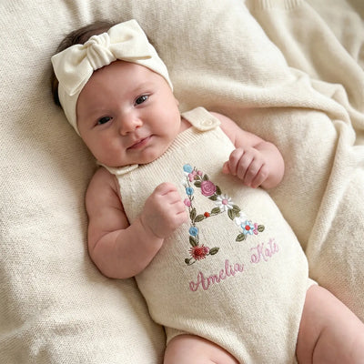 Baby wearing a cream-colored outfit with floral designs and text, lying on a soft beige surface.