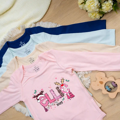 Pink baby onesie with embroidered design and text, placed on a wooden surface with flowers and toys.