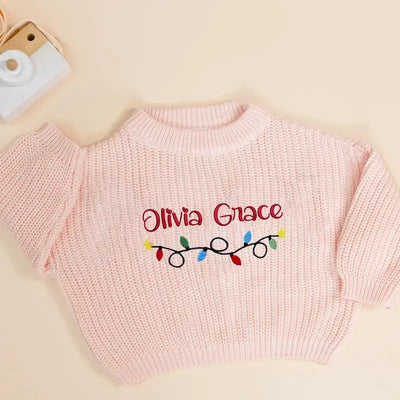 Pink sweater with 'Olivia Grace' and Christmas lights design on a beige background