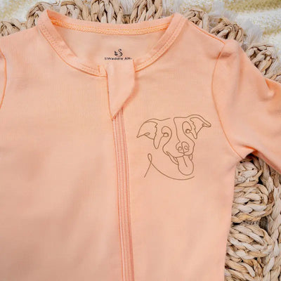 Peach-colored baby onesie with a dog illustration on a woven surface