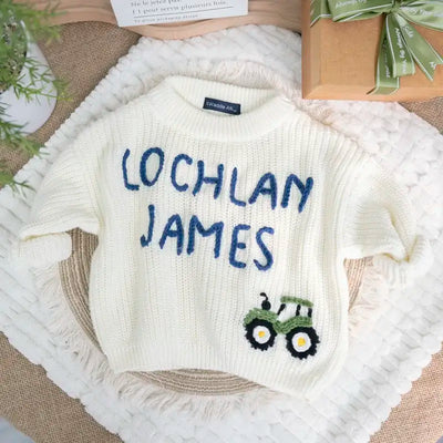 Baby sweater with embroidered name and tractor design on a textured surface