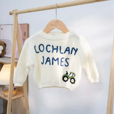 White sweater with 'Lochlan James' text and tractor design on a wooden hanger.