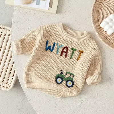 Beige sweater with 'Wyatt' and a tractor design on a light surface.