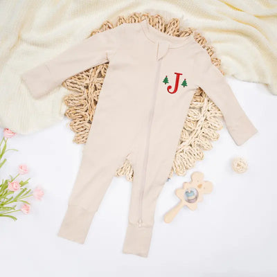 Beige baby outfit with 'J' monogram on a textured surface with flowers and a toy.