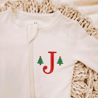 White baby onesie with red letter 'J' and green trees on a textured beige surface