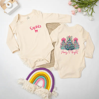 Two baby onesies with personalized names on a light surface with decorative items.