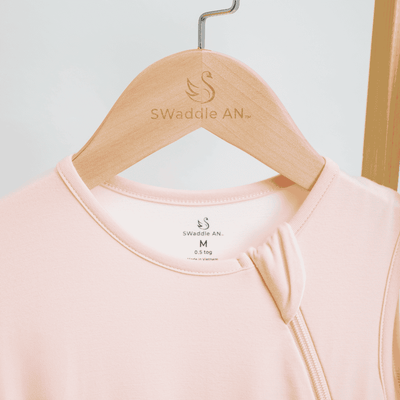 Pink baby garment on a hanger with 'Swaddle AN' branding.