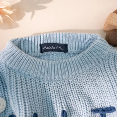 Close-up of a blue knitted sweater with a brand label on a light background