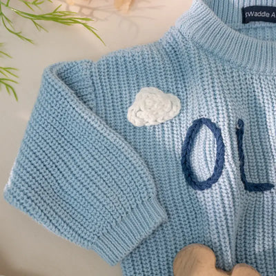 Light blue knitted sweater with a white cloud design and blue lettering on a light background