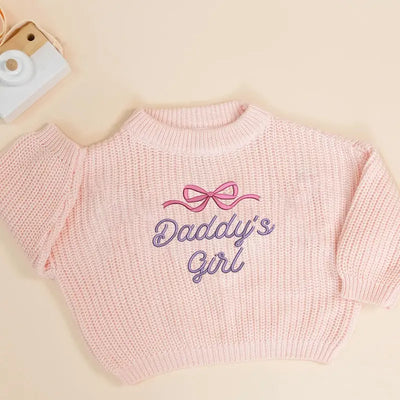 Pink sweater with 'Daddy's Girl' embroidery on a beige background