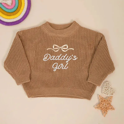 Brown knitted sweater with 'Daddy's Girl' text on a beige background