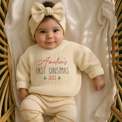Baby in a 'First Christmas 2025' outfit with a bow headband, sitting in a wicker basket.