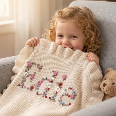 Child holding a knitted blanket with floral letters on a couch