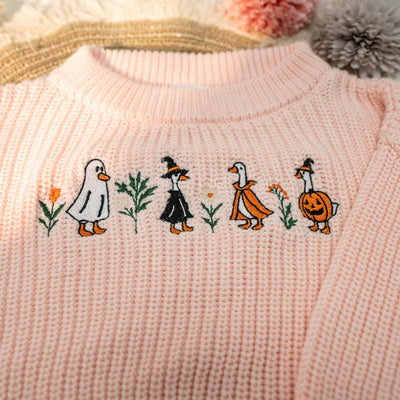 Embroidered design on a pink fabric with cartoon ducks in Halloween costumes.