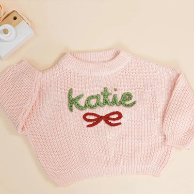Pink sweater with 'katie' and a red bow on a beige background