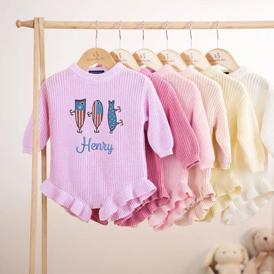 Row of baby sweaters on hangers with 'Henry' embroidered, against a neutral background.
