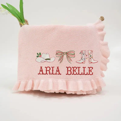 Pink pillow with embroidered designs and 'ARIA BELLE' text on a light background