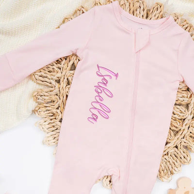 Pink baby onesie with 'Isabella' embroidered on it, placed on a textured surface.