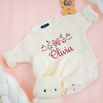 White baby romper with 'Olivia' embroidery on a pink background