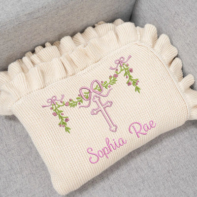 Cream-colored pillow with embroidered cross and floral design on a gray surface