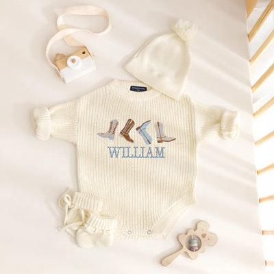 Baby romper with embroidered boots and name 'William' on a white surface.
