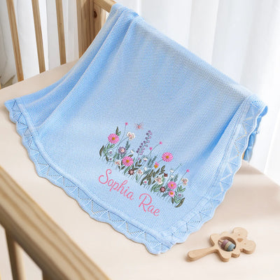 Light blue baby blanket with floral design and embroidered name on a wooden surface.