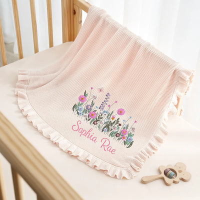 Pink baby blanket with floral design and embroidered name on a wooden chair.