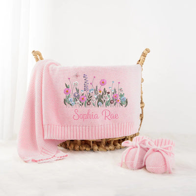 Pink baby blanket with floral embroidery and matching booties on a white background