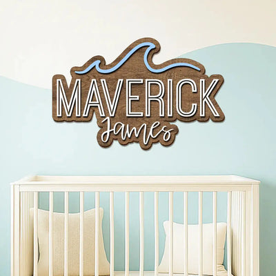 Wooden name sign with 'MAVERICK James' above a crib in a nursery.