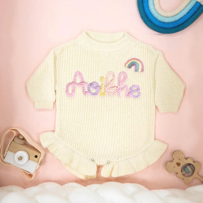 Cream baby romper with embroidered name on a pink background