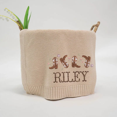 Beige personalized baby blanket with embroidered text and cowgirl boots design on a plain background
