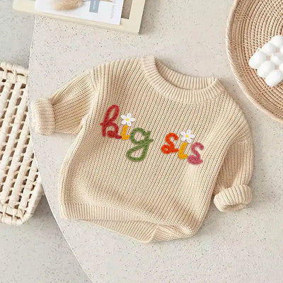 Beige baby sweater with 'big sis' text on a light surface