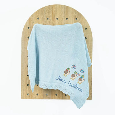 Light blue personalized baby blanket with embroidered patriotic mallard duck trio design and text on a wooden surface