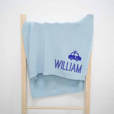 Light blue personalized baby blanket with 'William' and a police car design on a wooden ladder against a white background