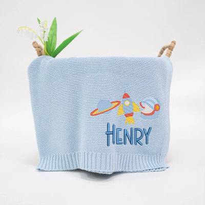 Light blue personalized baby blanket with a rocket space ship design and 'HENRY' text on a white background