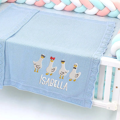 Blue personalized baby blanket with embroidered geese and name 'Isabella' on a crib.
