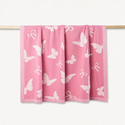Pink blanket with white butterfly patterns on a wooden rod against a white background