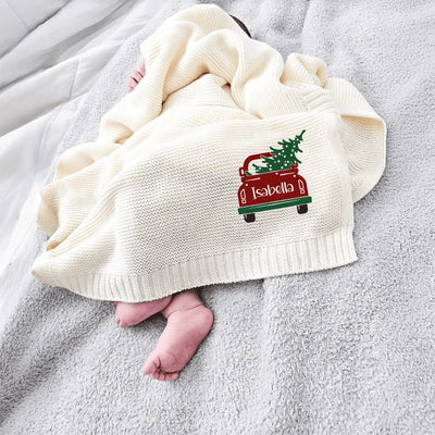 Baby wrapped in a cream personalized baby blanket with a Christmas tree in the car design, lying on a gray surface.