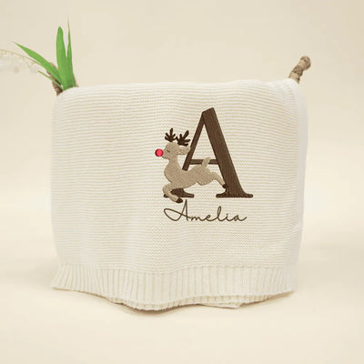 Cream personalized baby blanket with a reindeer design and the name 'Amelia' on a beige background