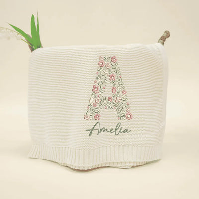 Cream personalized baby blanket with initals floral letter 'A' and name 'Amelia' on a beige background
