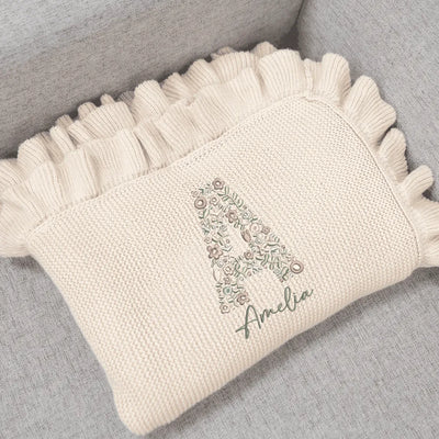 Cream personalized baby blanket with initials floral design and embroidered name on a gray surface