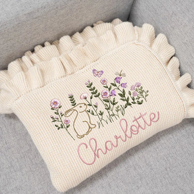 Cream Personalized baby blanket with bunny floral design and 'Charlotte' text on a gray surface