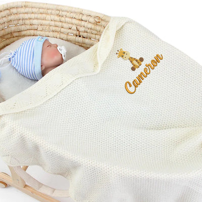 Newborn baby wrapped in a cream personalized blanket with 'Cameron' embroidered, lying in a wooden crib.