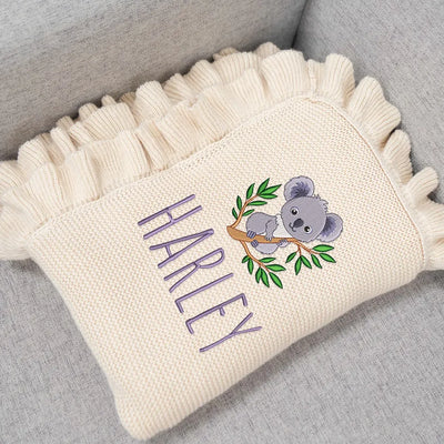 Cream personalized baby blanket with embroidered koala and 'Harley' on a gray surface